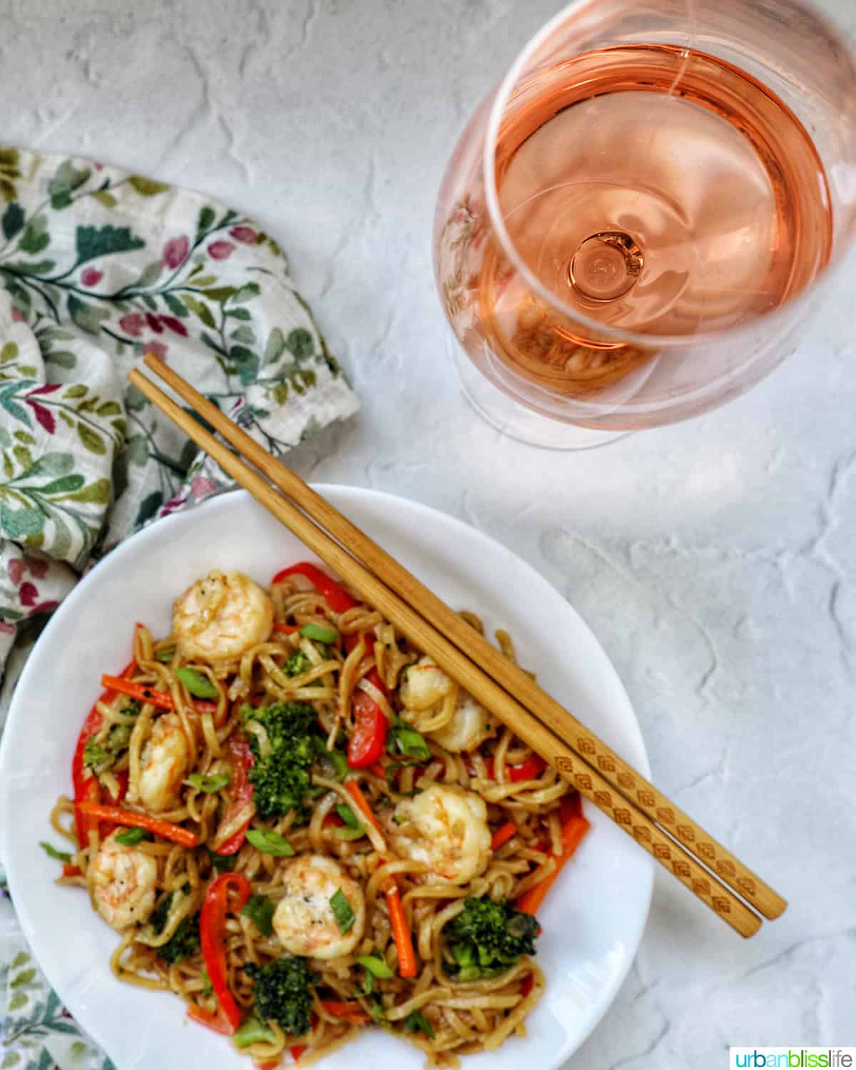 white bowl of bowl of prawn chow mein noodles with a glass of rosé.