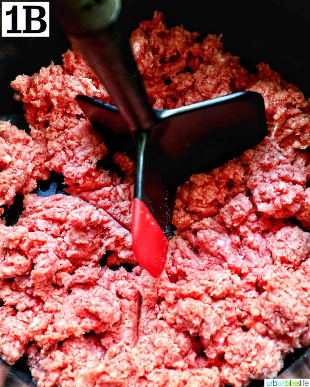 ground beef in an air fryer basket with a meat chopper.