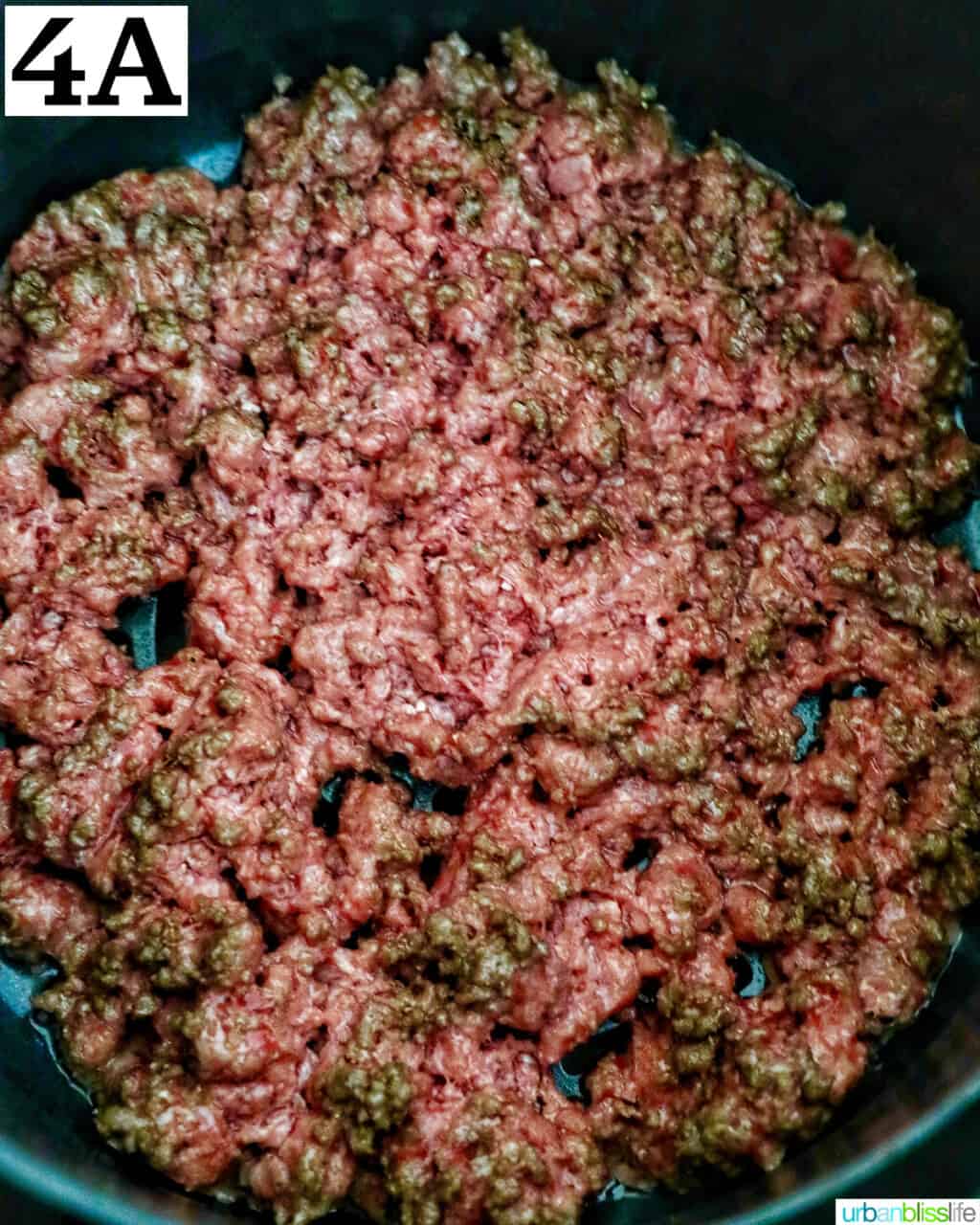 ground beef cooking in an air fryer basket.