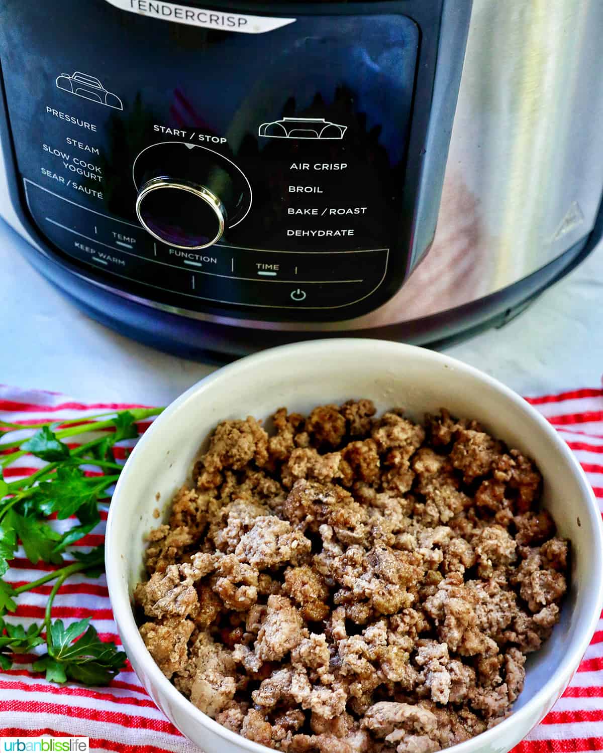 air fryer and ground beef in a white bowl with parsley sprigs around it and a red and white striped towel.