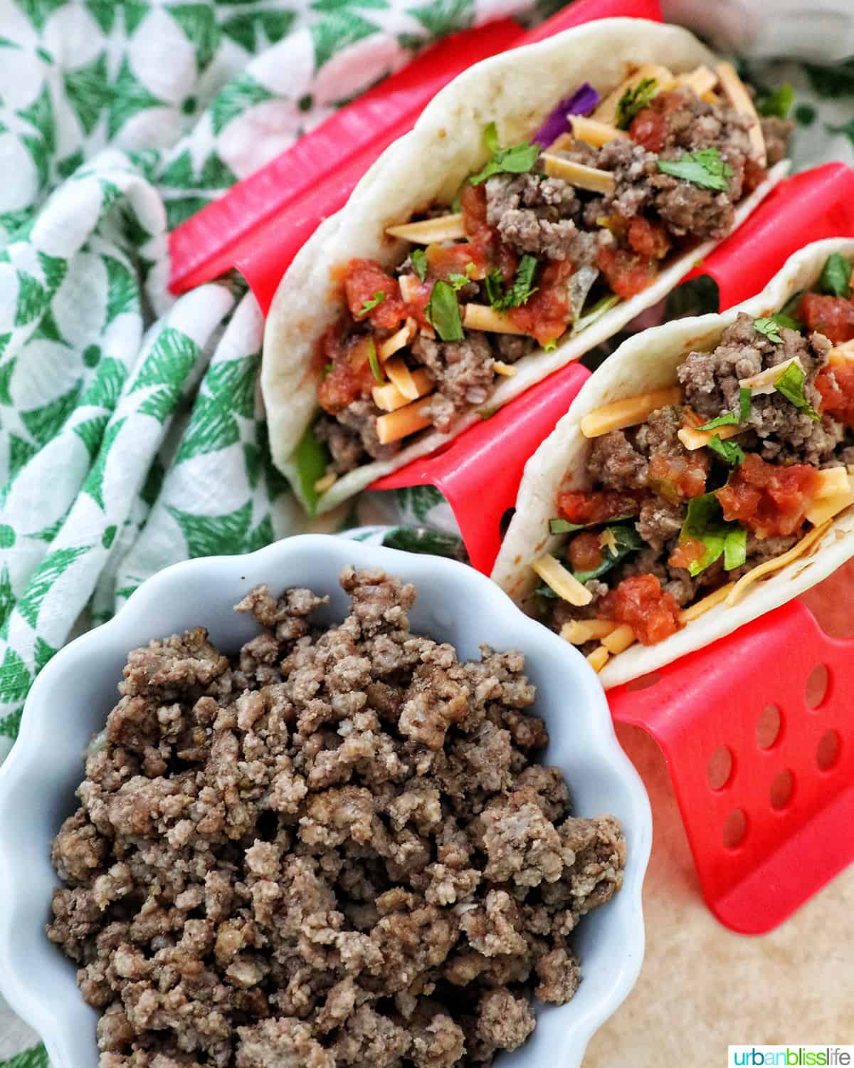 white bowl with ground beef in front of a red taco holder holding two beef tacos.