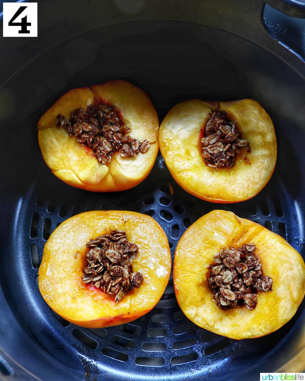 halved peaches with cinnamon oats topping in an air fryer basket.