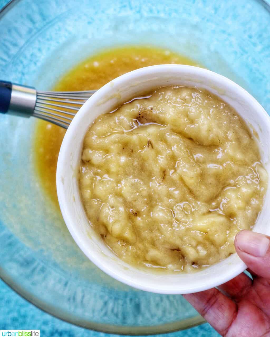bowl of mashed bananas over a clear mixing bowl of other ingredients.