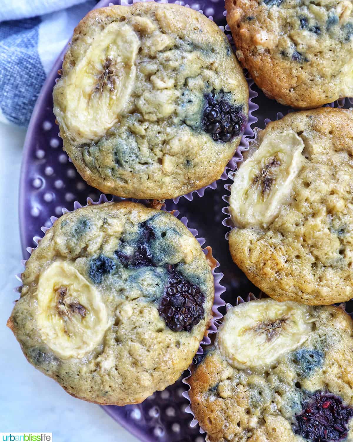 purple plate with several banana blackberry oatmeal muffins on top.