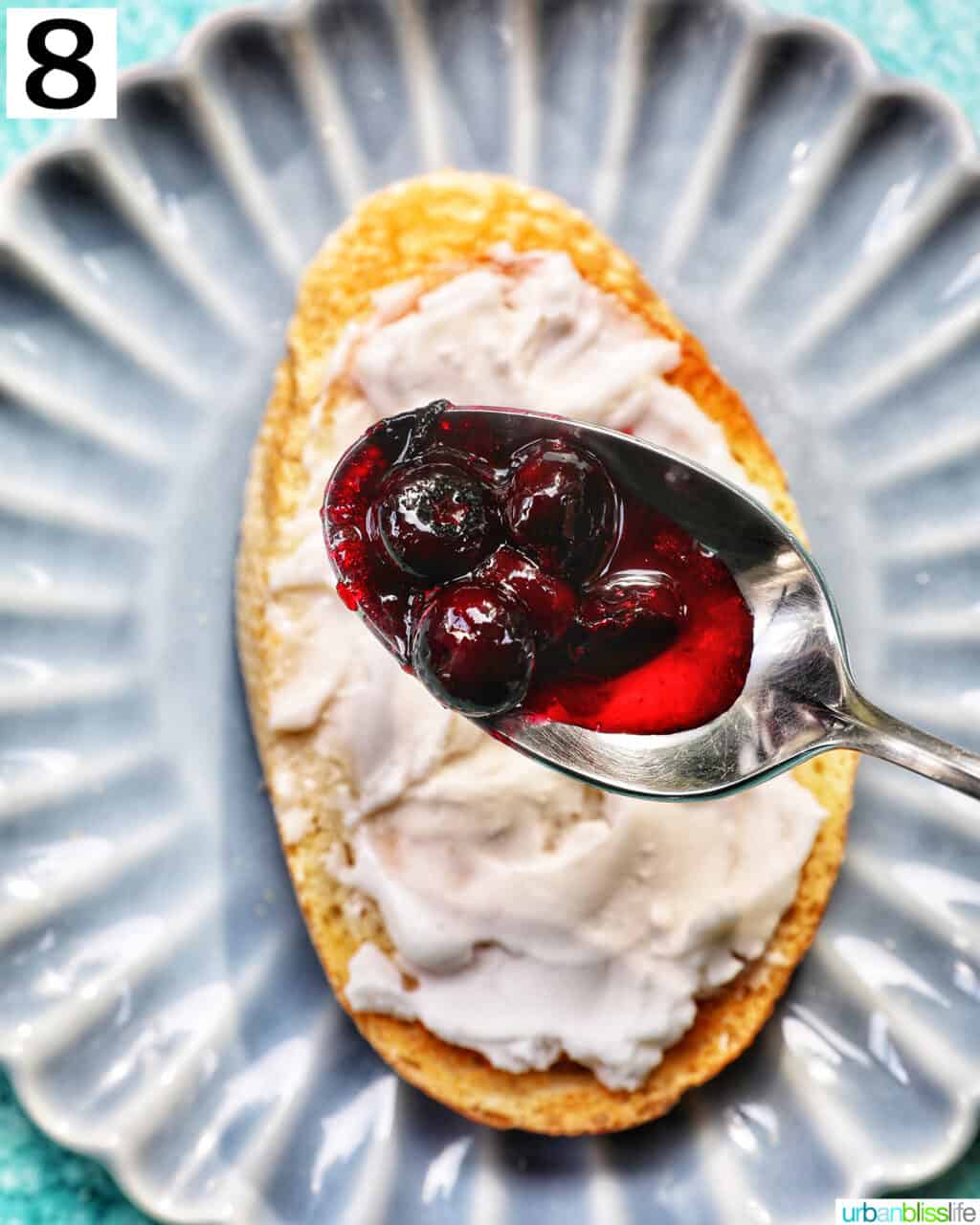 spoon full of blueberry compote over a piece of toast with cream cheese spread on a blue plate.