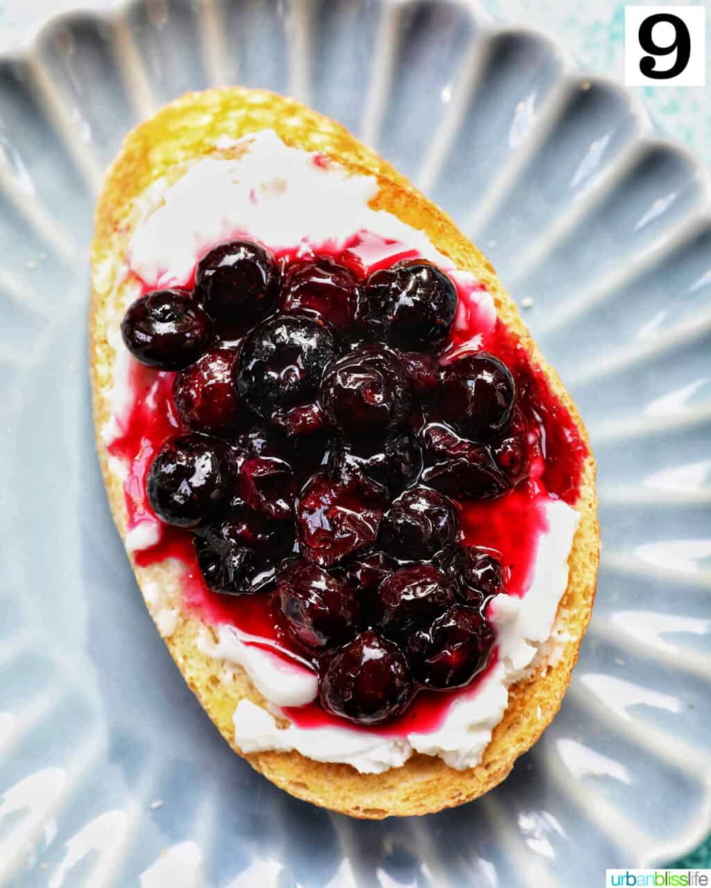 blueberries and cream cheese on toast on a blue scalloped plate.
