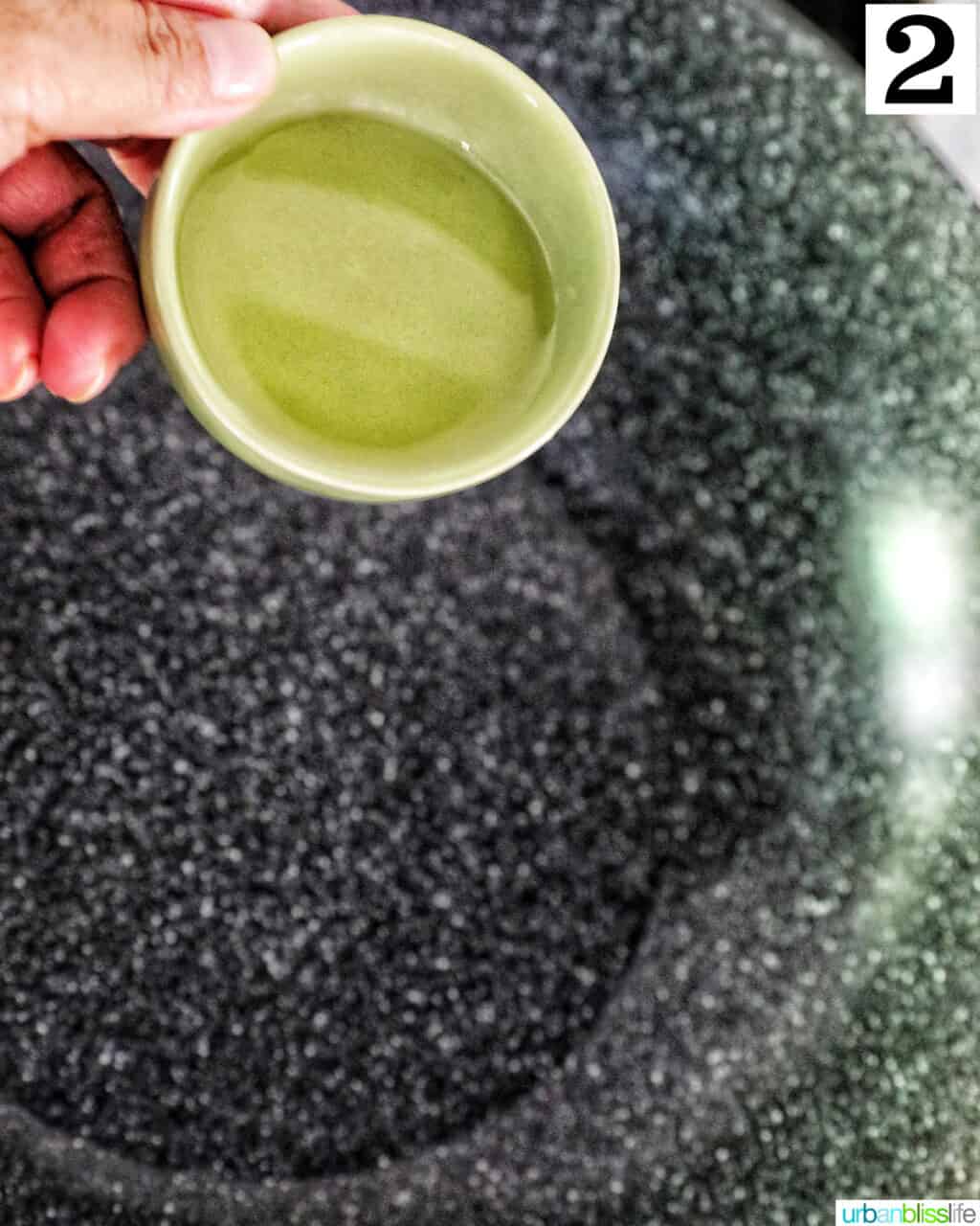 hand holding a small bowl of vegetable oil over a wok.