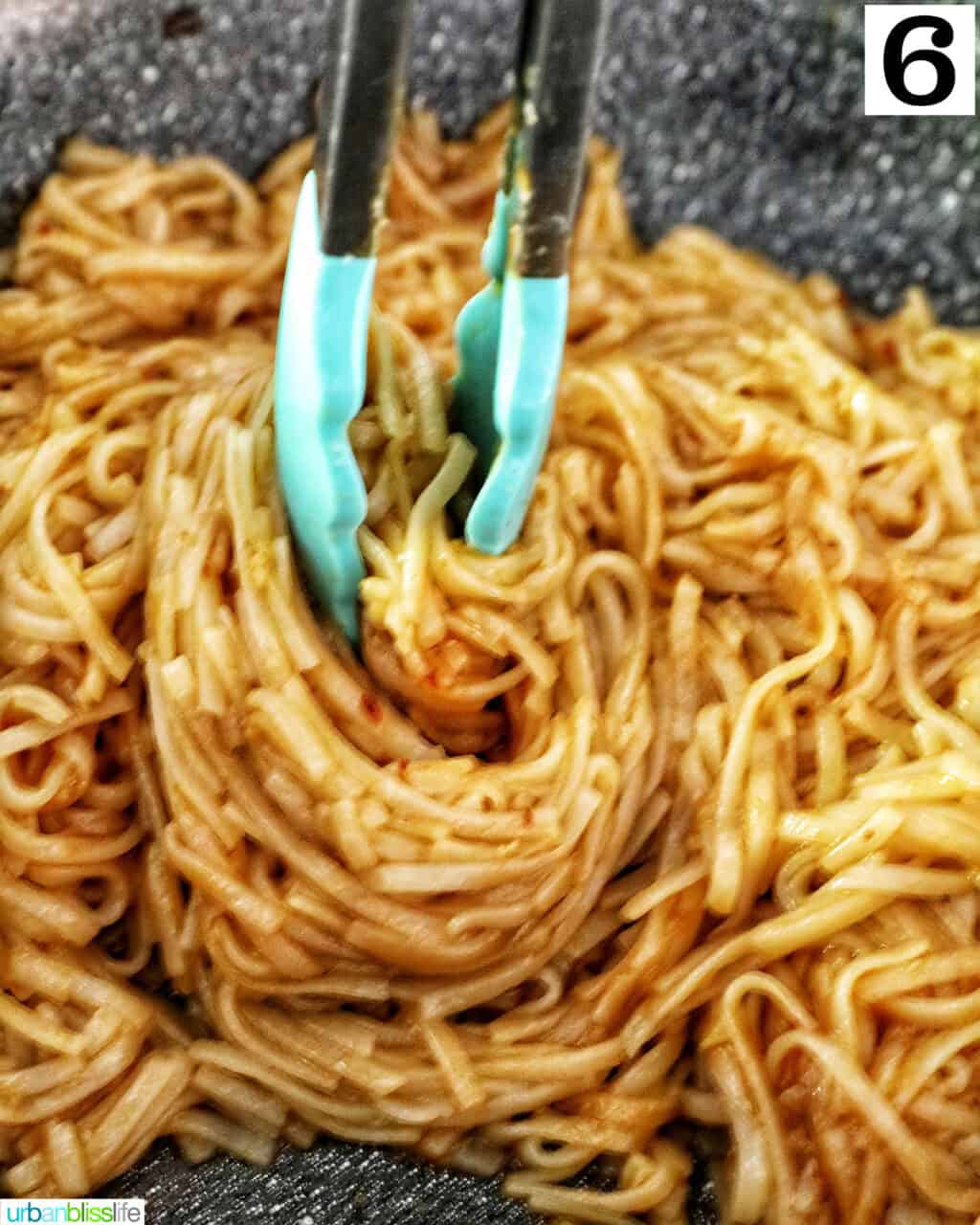 blue tongs twirling Chili Garlic Noodles in a wok.