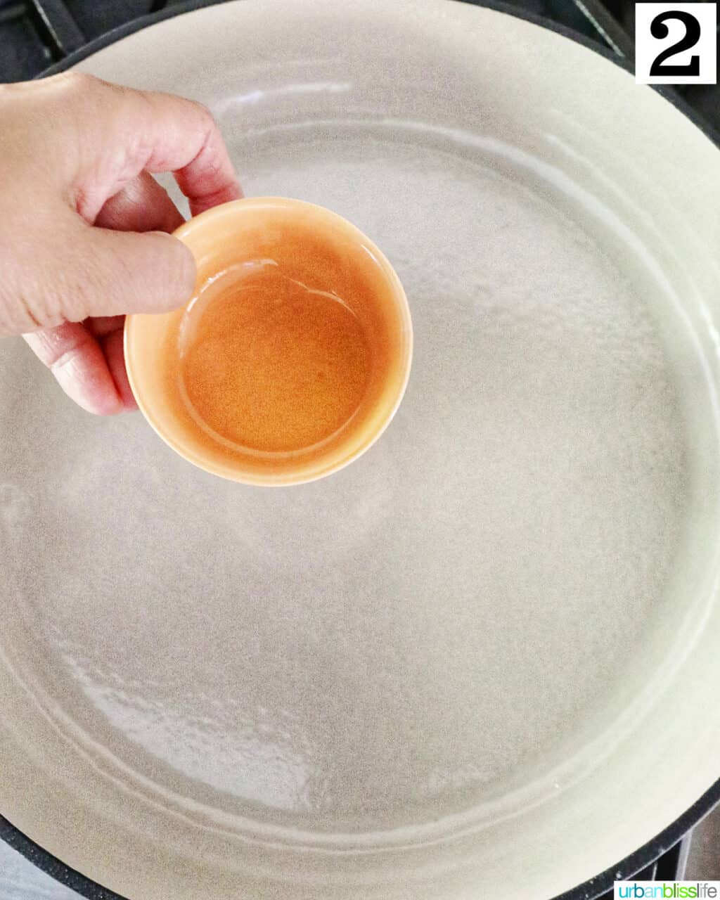 hand holding oil over a large skillet.