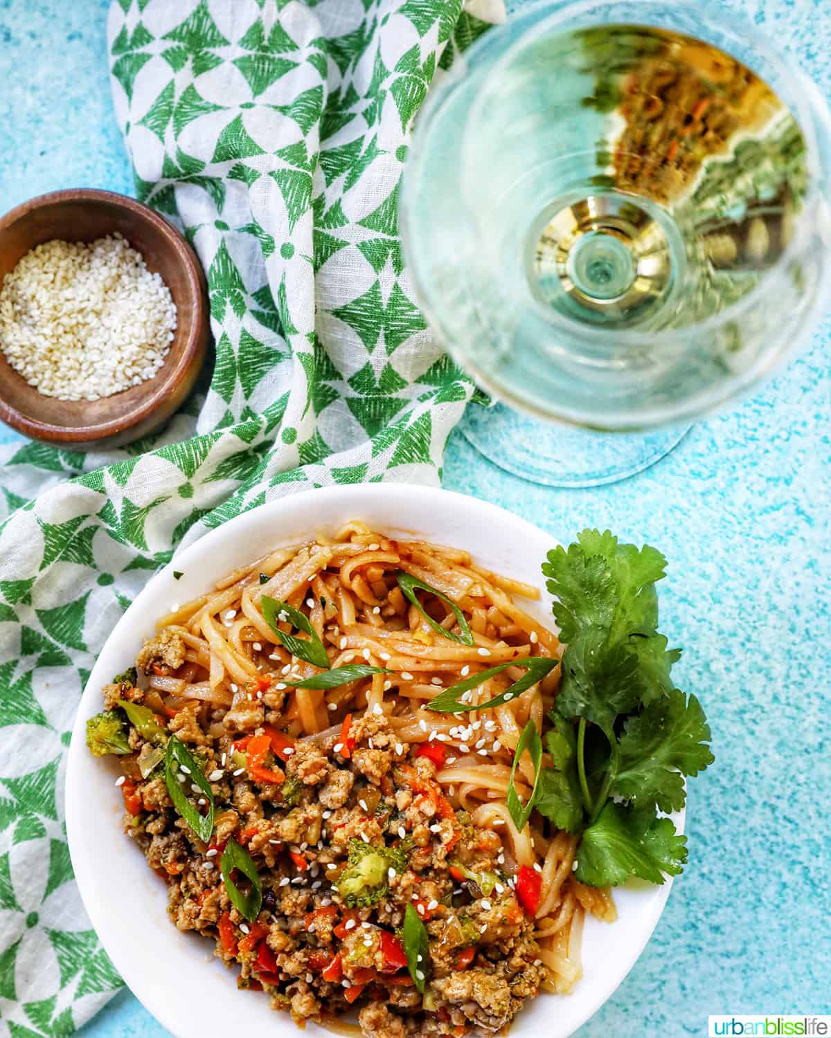 Ground Turkey Teriyaki with green onions, broccoli, carrots, and red bell peppers, in a white bowl with cilantro garnish with glass of white wine.