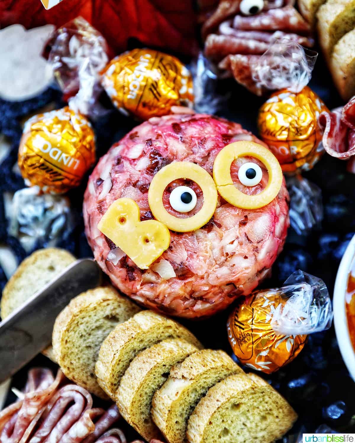 Halloween Charcuterie Board with charcuterie meats, cheeses, crackers, jams, pretzels, fruits, candy eyes, and more orange, purple, and black food.