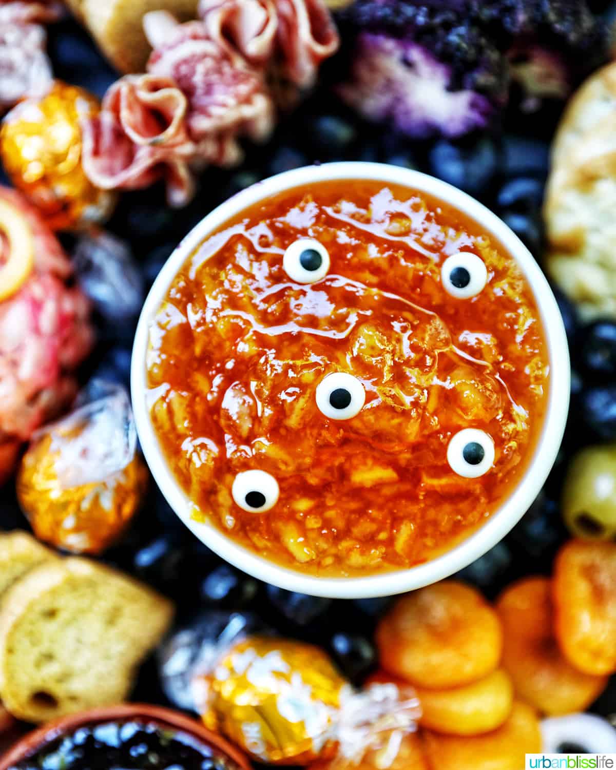 Halloween Charcuterie Board with charcuterie meats, cheeses, crackers, jams, pretzels, fruits, candy eyes, and more orange, purple, and black food.