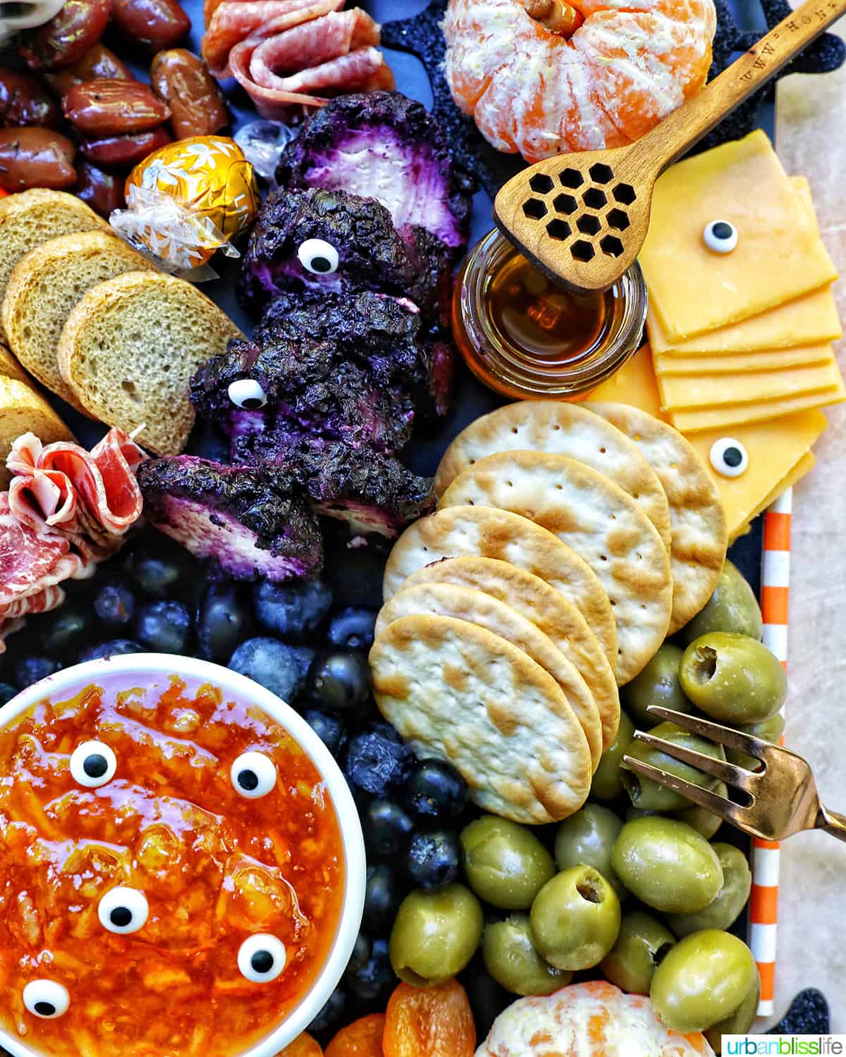 Halloween Charcuterie Board with charcuterie meats, cheeses, crackers, jams, pretzels, fruits, candy eyes, and more orange, purple, and black food.