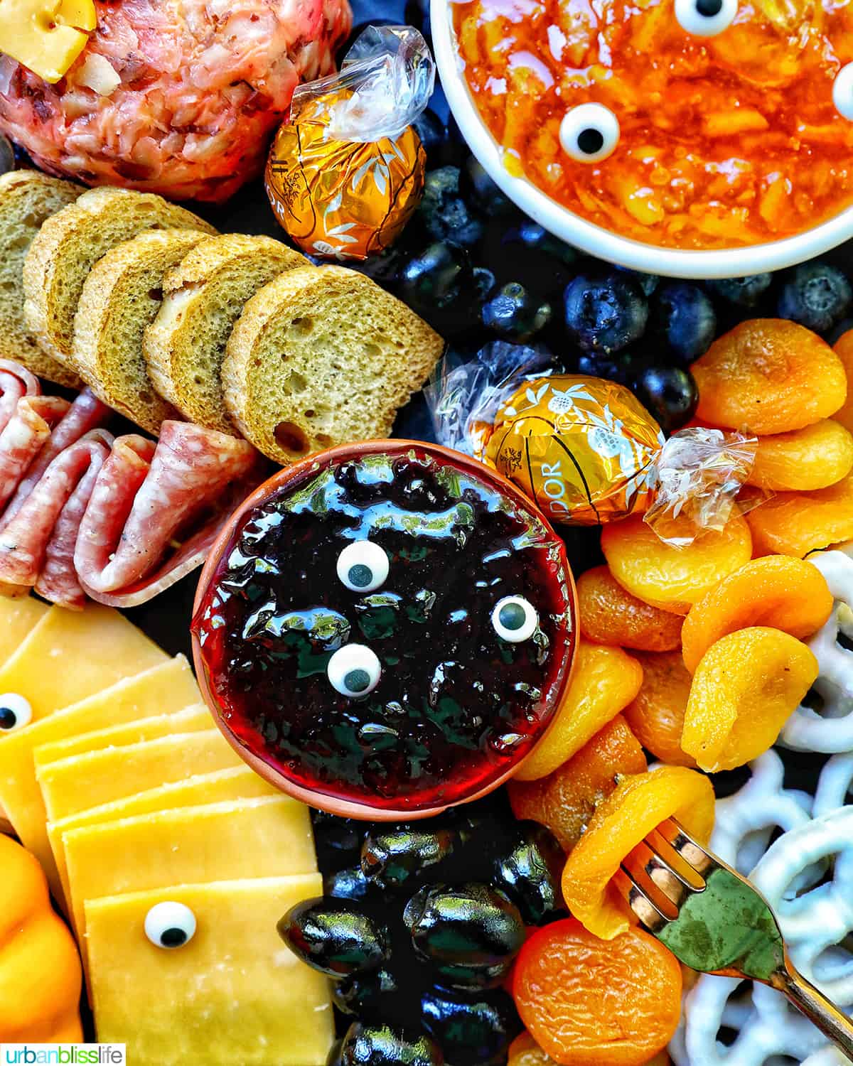 Halloween Charcuterie Board with charcuterie meats, cheeses, crackers, jams, pretzels, fruits, candy eyes, and more orange, purple, and black food.