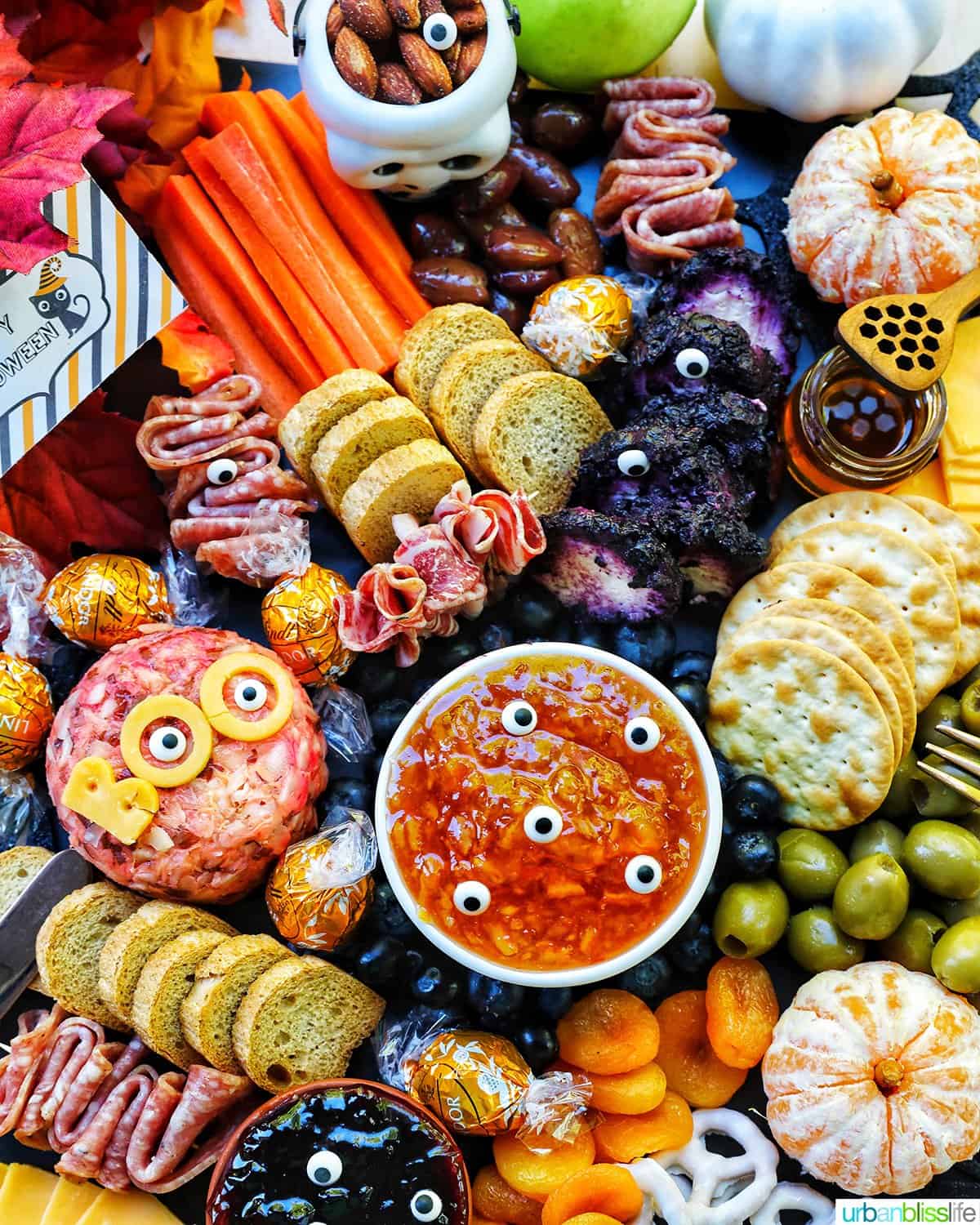 Halloween Charcuterie Board with charcuterie meats, cheeses, crackers, jams, pretzels, fruits, candy eyes, and more orange, purple, and black food.
