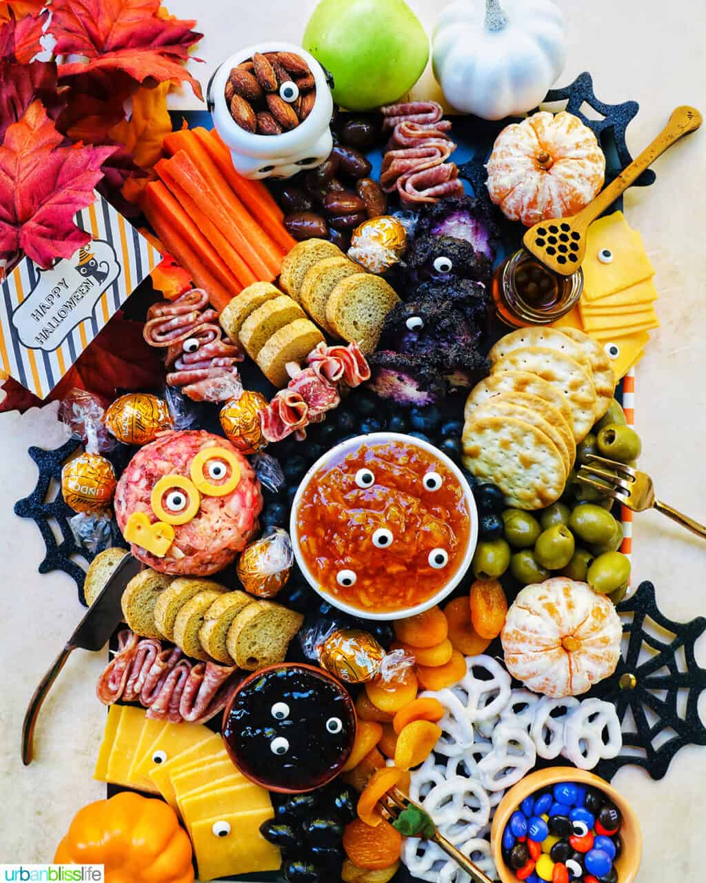 Halloween Charcuterie Board with charcuterie meats, cheeses, crackers, jams, pretzels, fruits, candy eyes, and more orange, purple, and black food.