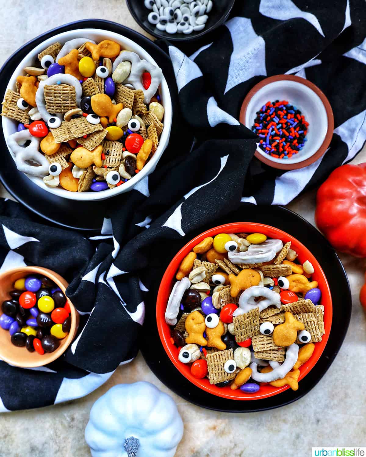 two bowls of Halloween Snack Mix on a black and white napkin with small bowls of candy on the side.