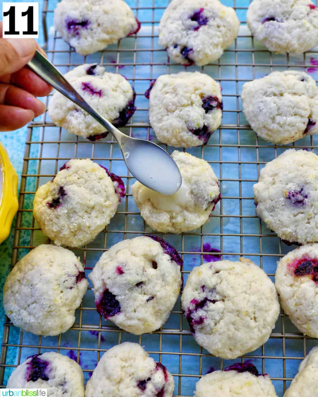 spoon of lemon glaze over lemon blueberry cookies on a wire rack with white and blue napkin.