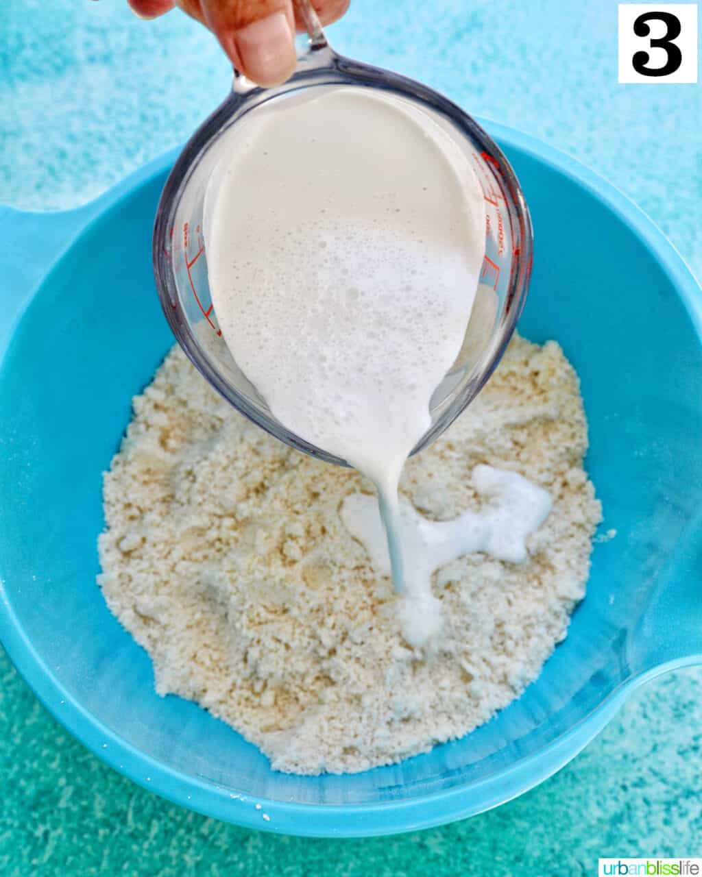 pouring cream into a blue bowl of dry ingredients to make lemon blueberry cookies.