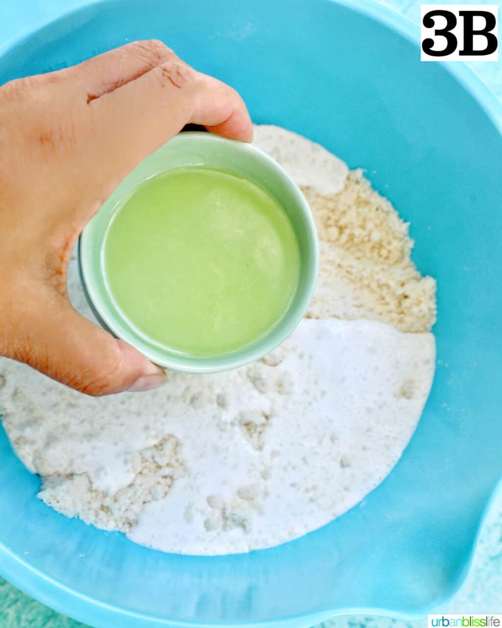 hand holding lemon juice over dry ingredients to make lemon blueberry cookies.
