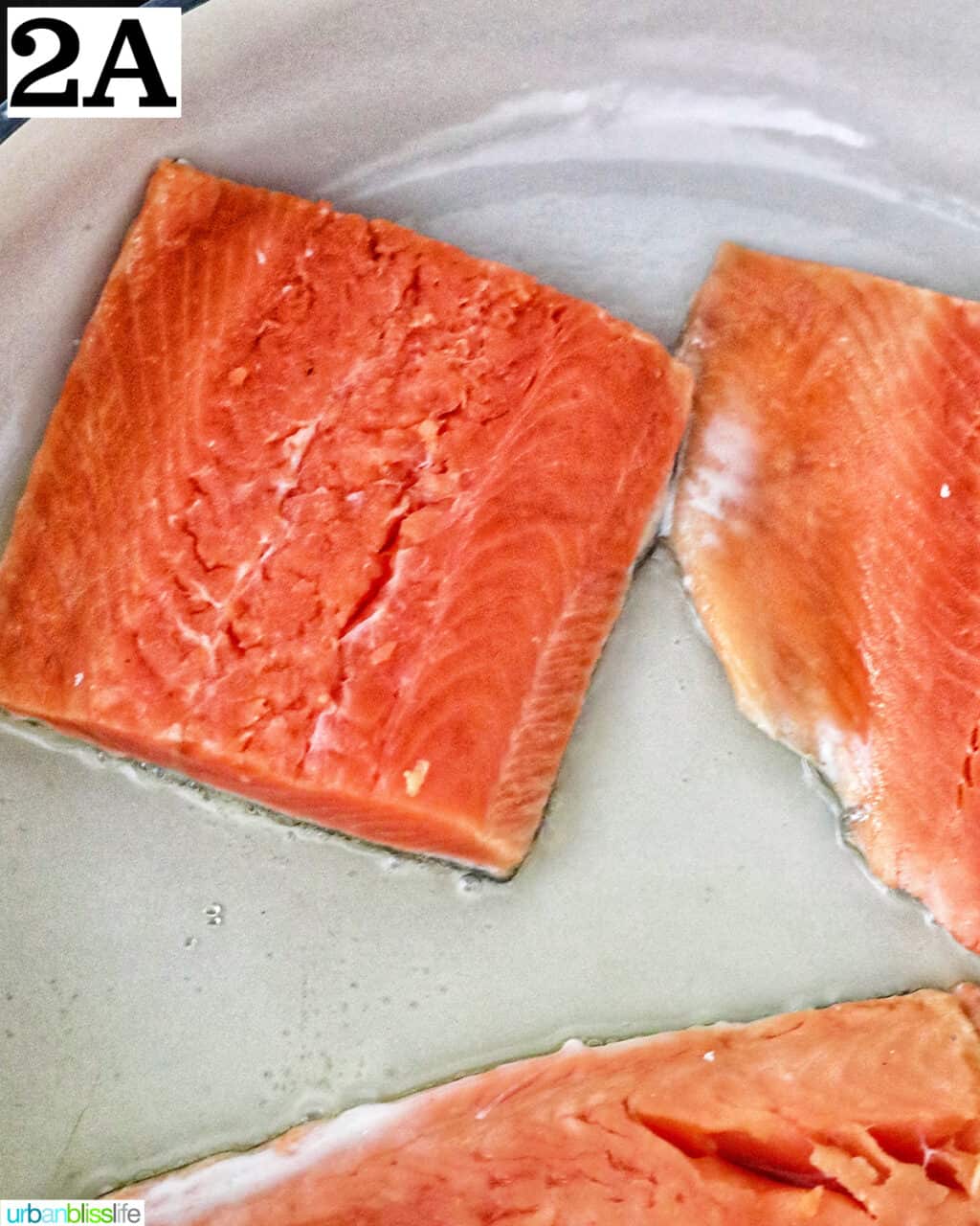 uncooked salmon cooking in a large white skillet.
