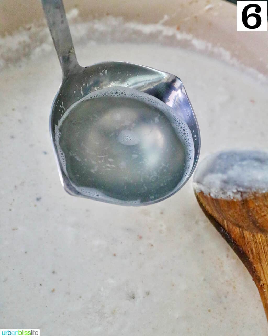 ladle full of hot starchy pasta water over a large skillet with cream sauce.