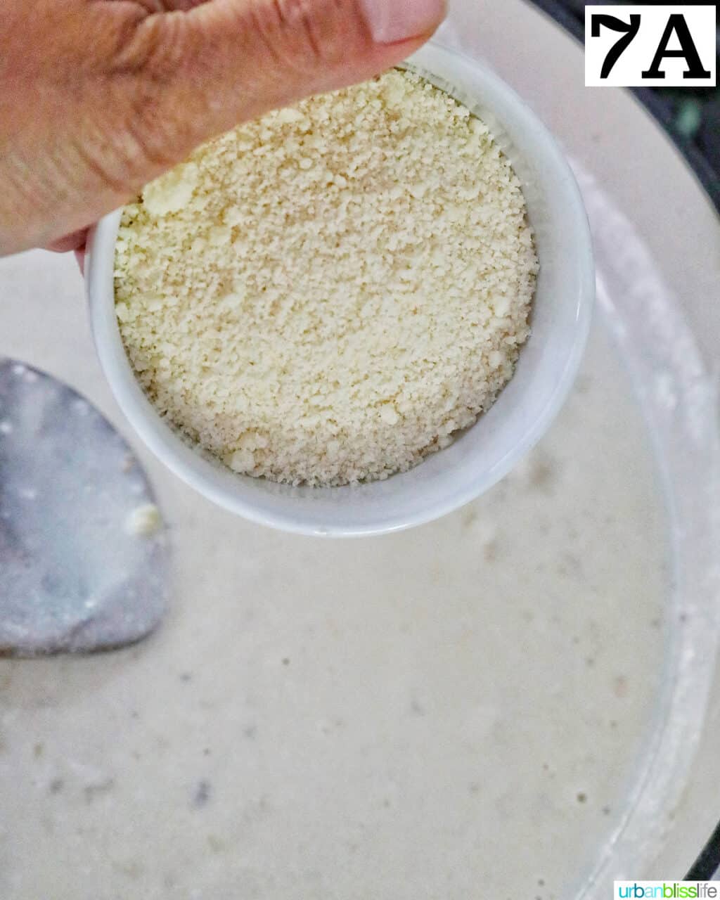 hand holding a bowl of grated parmesan cheese over cream sauce in a skillet.