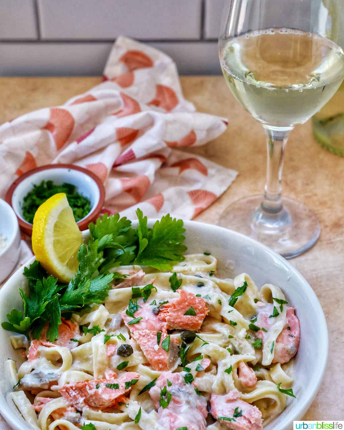 pasta alla salmone with garnishes of parsley and lemon slices in a white bowl with glass of white wine.