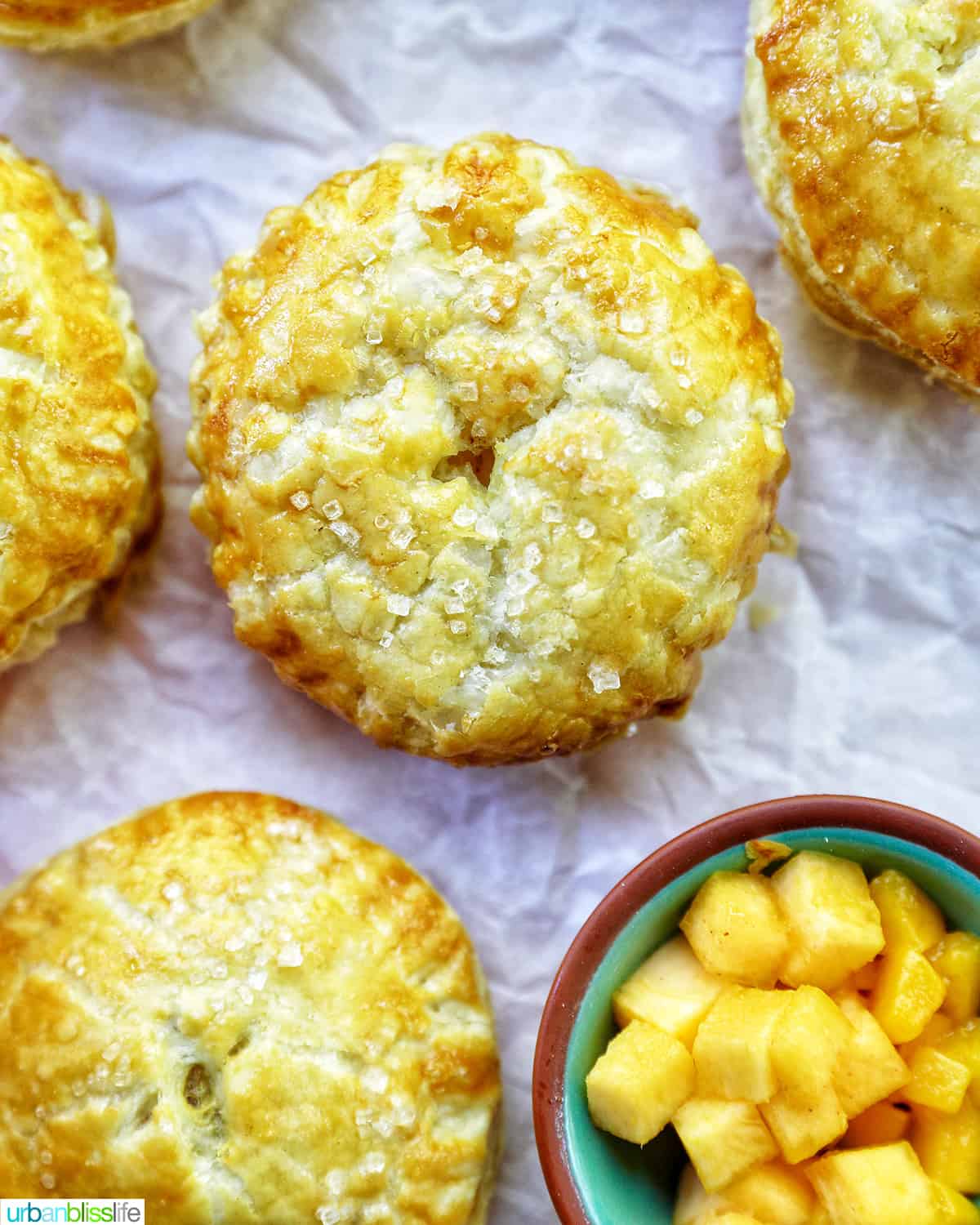 several mini peach mango hand pies on crinkled parchment paper with a bowl of diced peaches and mangoes.