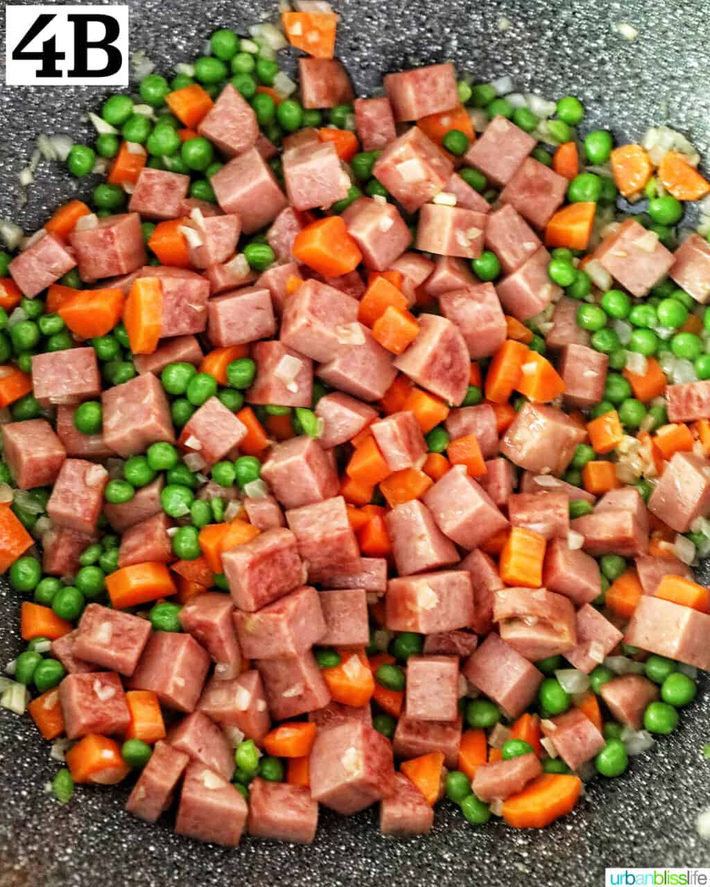 cooking cubed spam, garlic, onions, peas, and carrots in a wok.