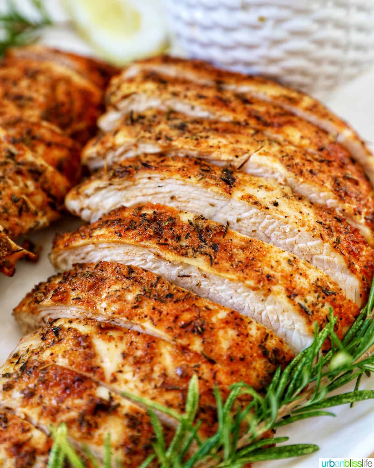 two sliced turkey tenderloins on a plate with fresh herbs and lemon slices.