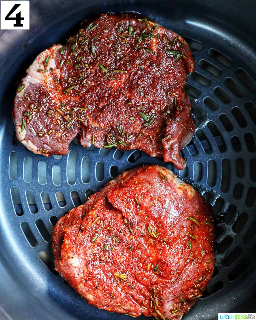 two raw seasoned filet mignon steaks in an air fryer basket.