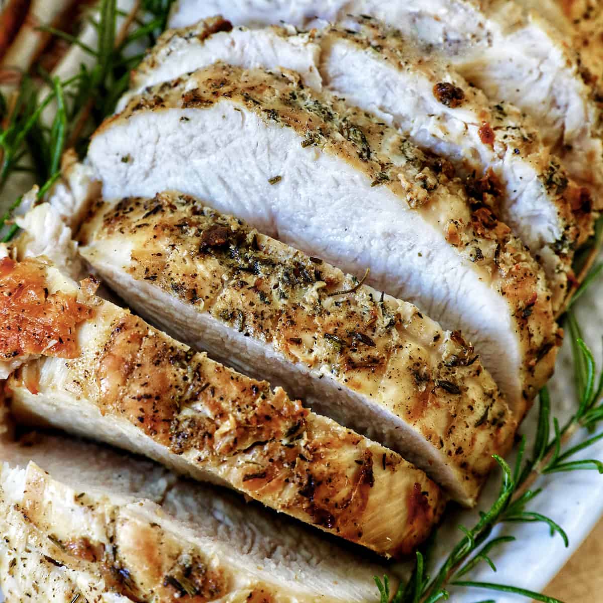 sliced turkey breast with rosemary sprigs on a plate.