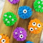 several colorful bright halloween monster cupcakes on a wood board.