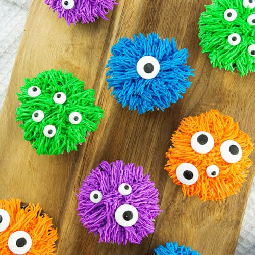 several colorful bright halloween monster cupcakes on a wood board.