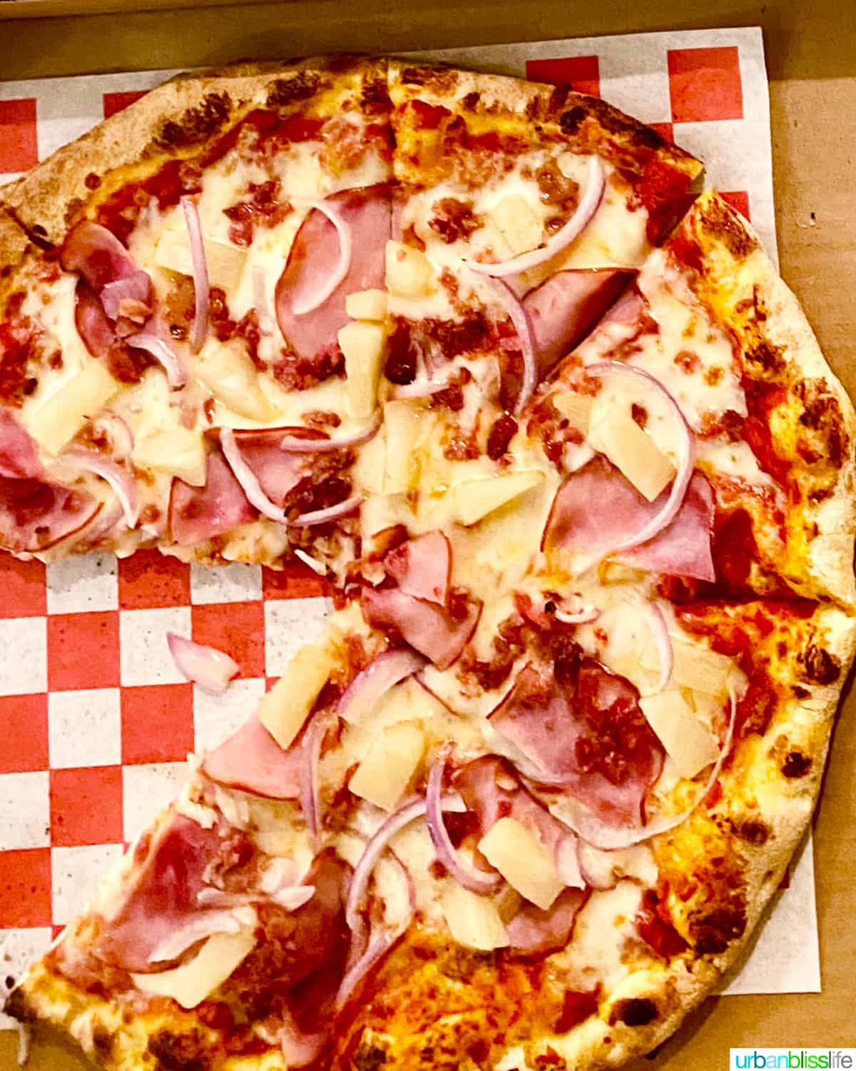 hawaiian pizza on a red and white checkered paper in a pizza box.