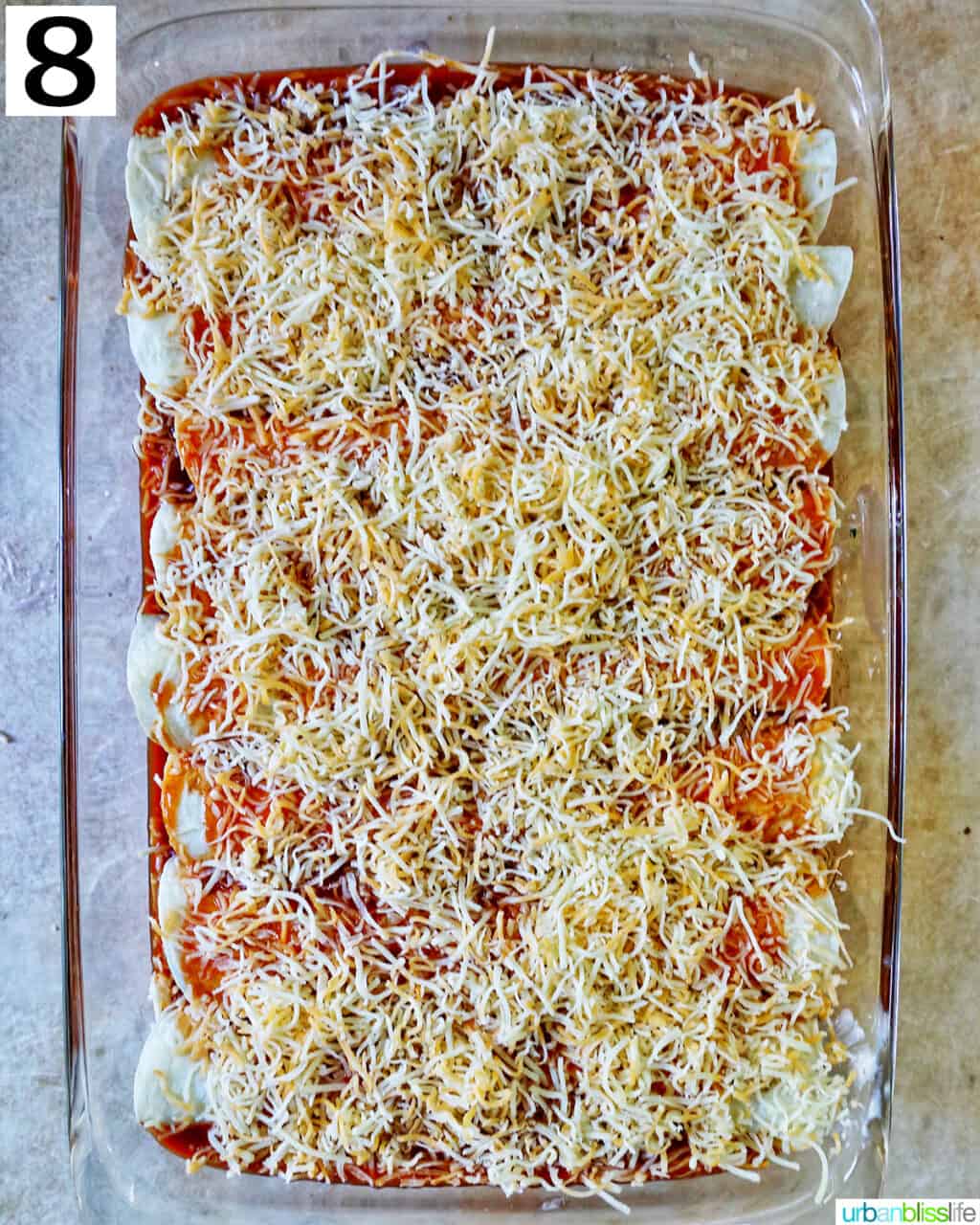 layer of shredded cheese on top of rolled and sauced enchiladas in a casserole dish.