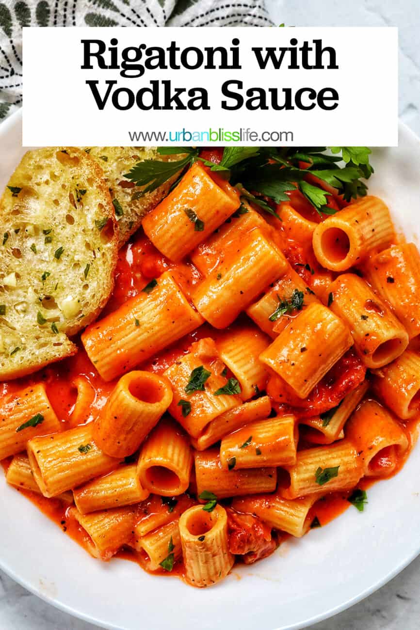 white bowl with rigatoni with vodka sauce and side of garlic bread and parsley with title text.