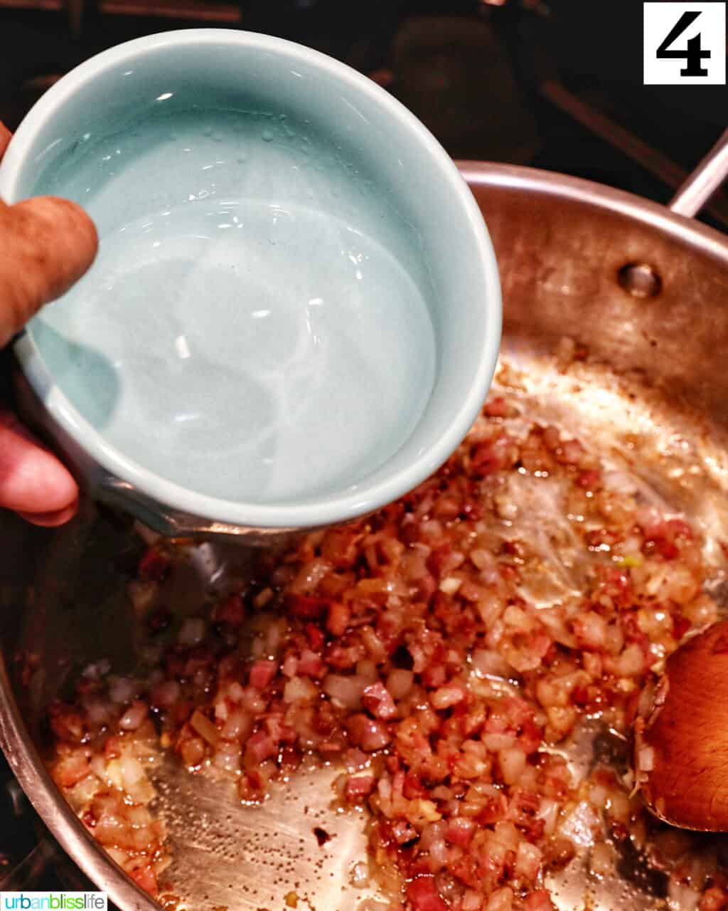 hand pouring a bowl of vodka into a large saucepan with bacon, onions, and garlic.