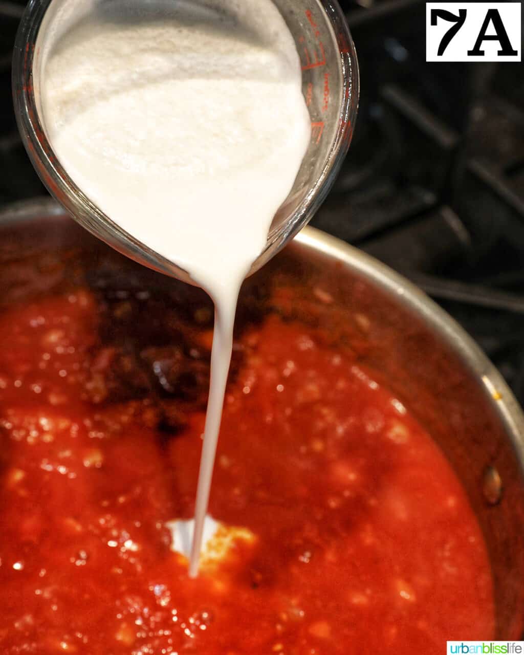 pouring cream into a saucepan with tomato sauce.