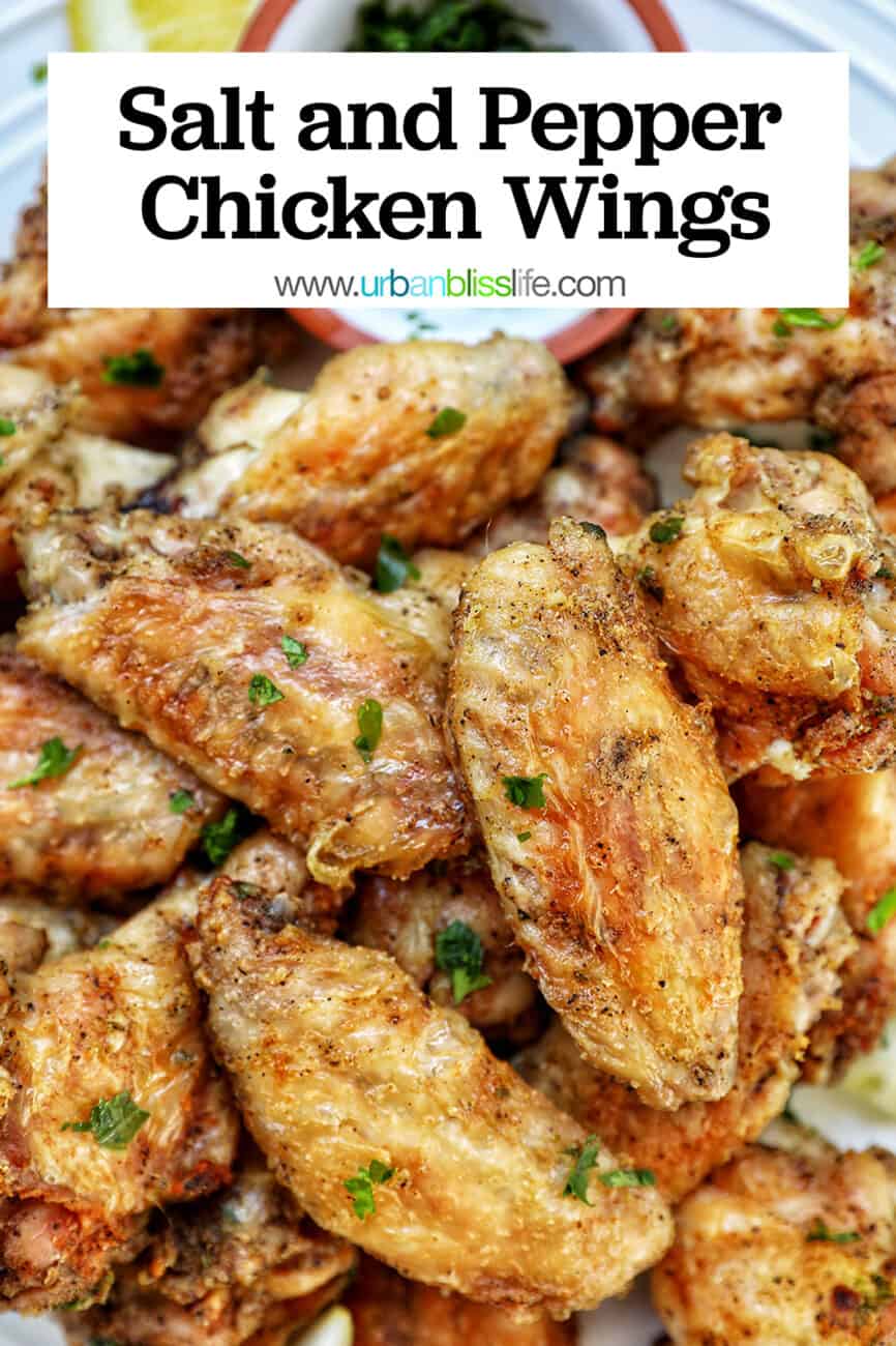 white plate full of salt and pepper wings with side of chopped fresh parsley and lemon wedges with title text that reads "Salt and Pepper Chicken Wings"