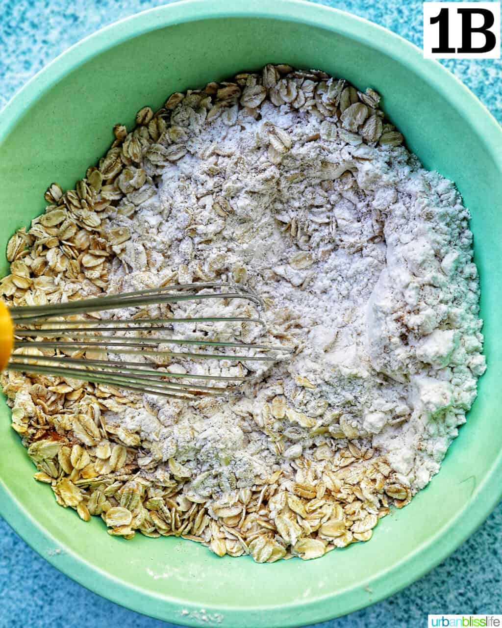 dry ingredients for cookie batter in a green bowl with whisk.