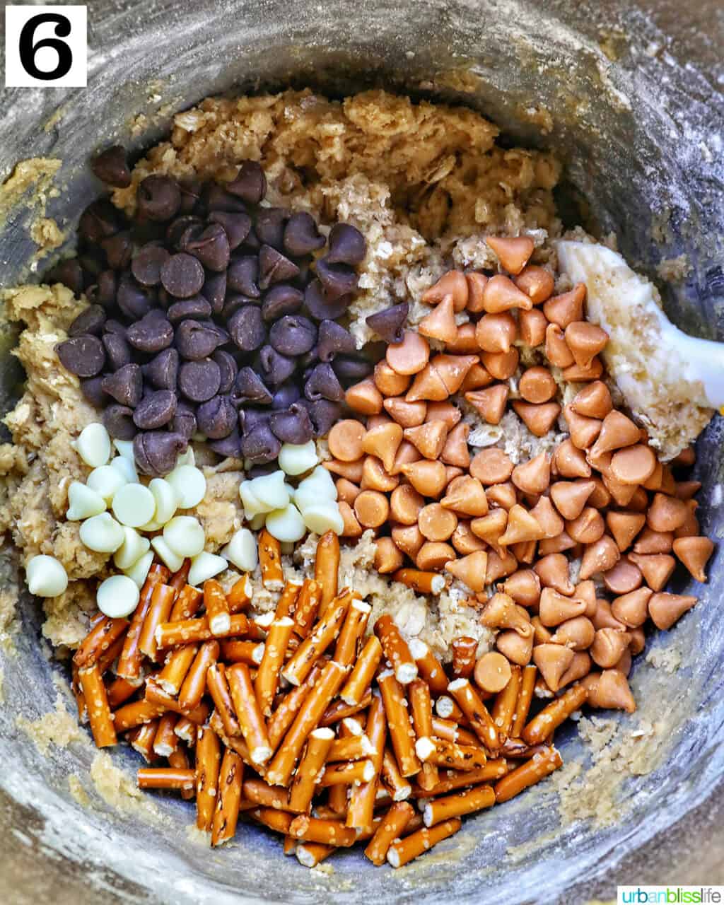 chocolate chips and pretzels added to cookie dough batter in a stand mixer bowl.