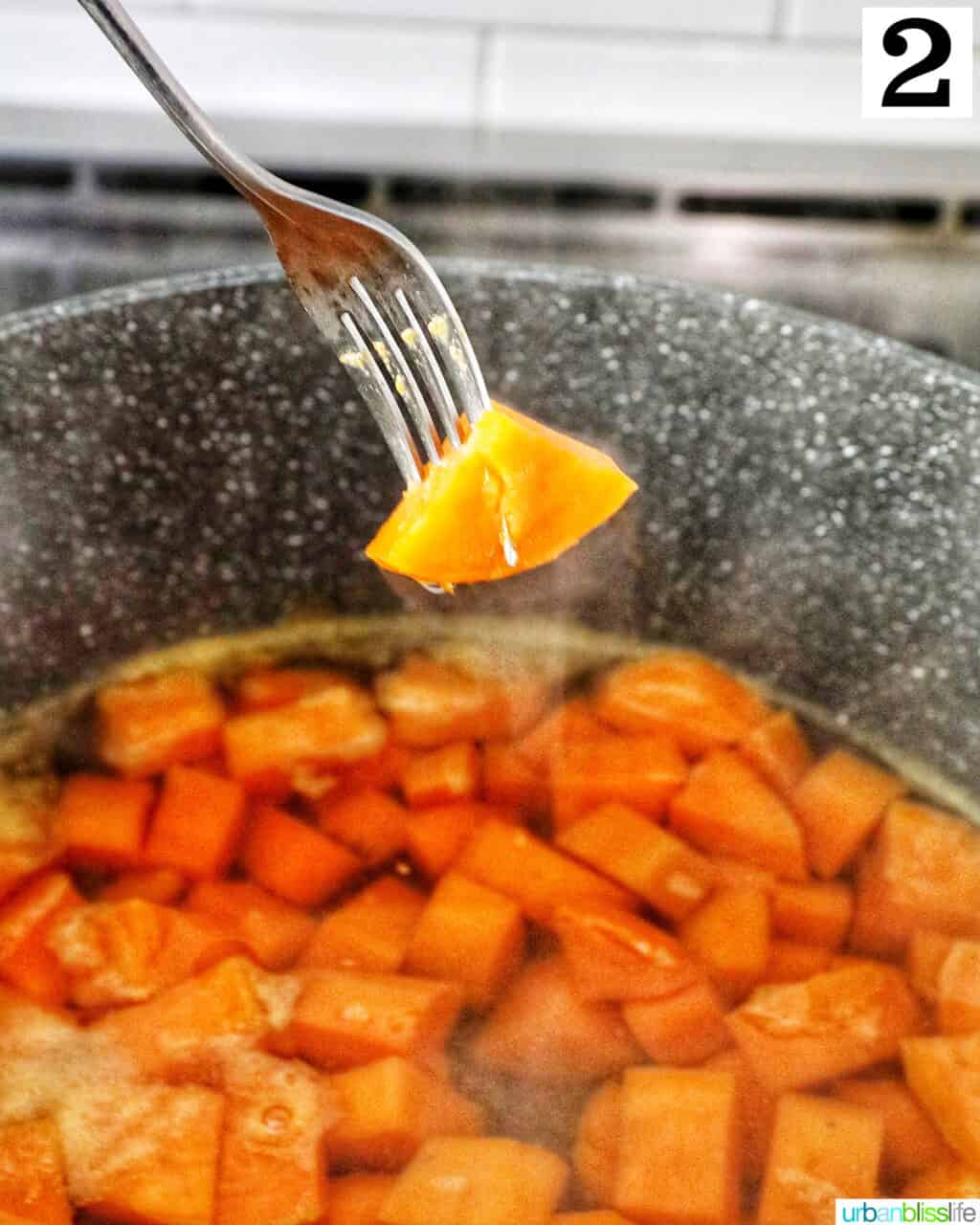 Fork holding up a piece of sweet potato above a large pot.