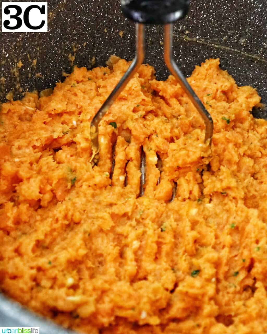 potato masher mashing up sweet potatoes in a large pot.