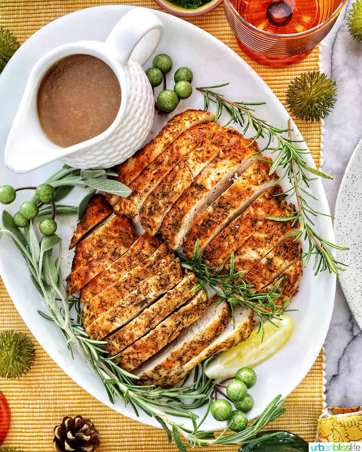 two sliced turkey tenderloins on a plate with fresh herbs and lemon slices and gravy and bottle of wine.