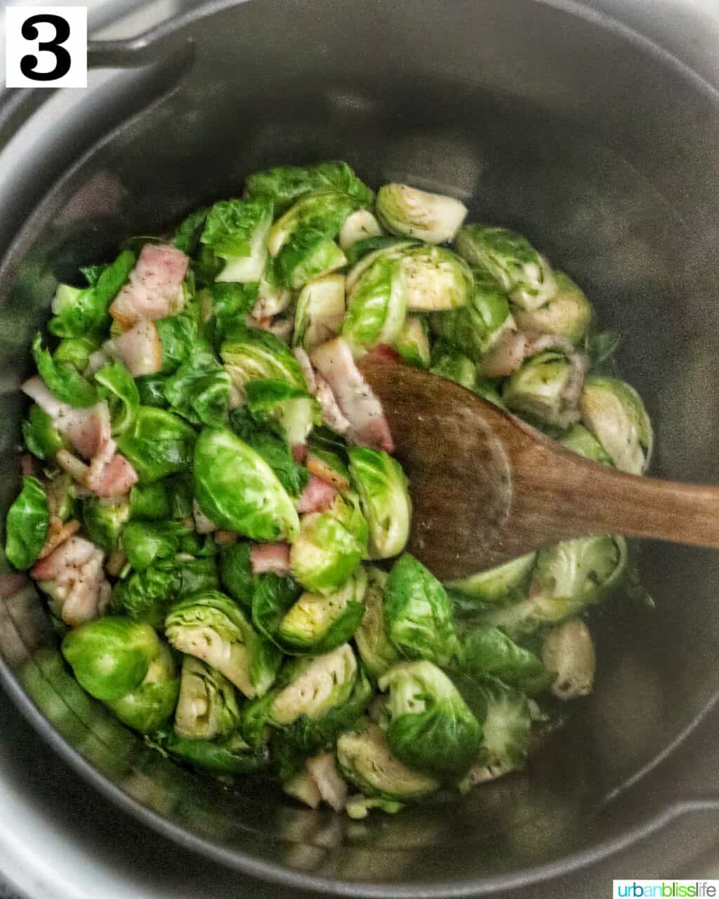bowl of brussels sprouts with bacon in an air fryer basket with wooden spoon.