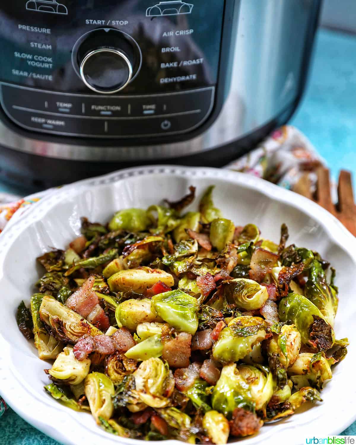 bowl of brussels sprouts with bacon in front of an air fryer.