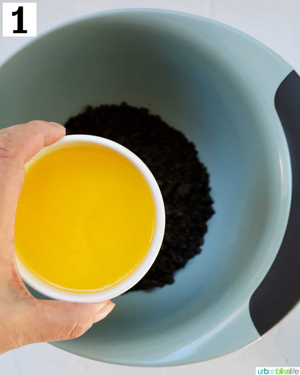 hand holding butter over a bowl of crushed oreos.
