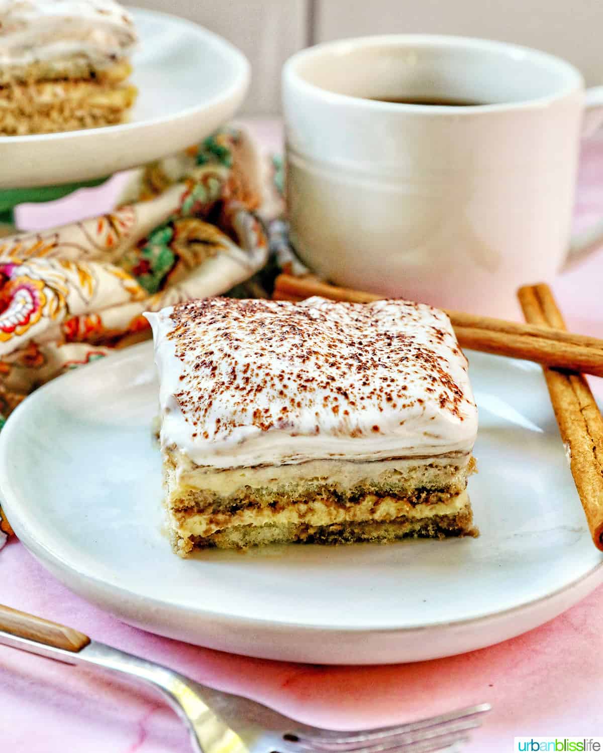 slice of dairy free tiramisu dessert on a white plate with cup of coffee behind it.